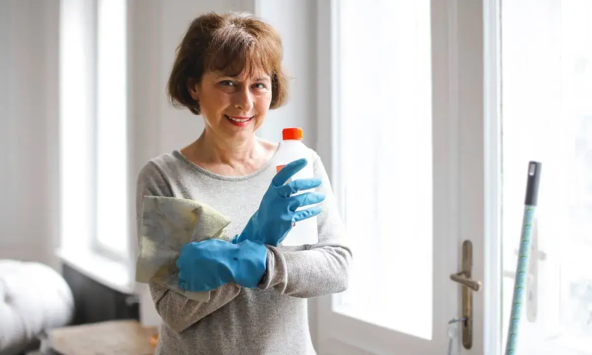 Mujer con guantes azules, paño y botella de limpiador, lista para saber como limpiar un colchon de viscoelastica.