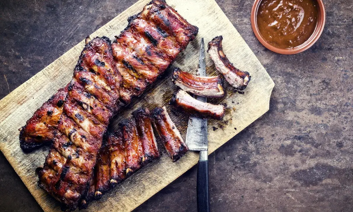 Soczyste żeberka w miodzie, grillowane do perfekcji, leżą na desce obok sosu.