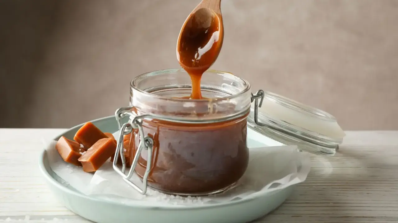 En träsked droppar krämig kolasås ner i en burk. Perfekt för ditt kolasås recept!