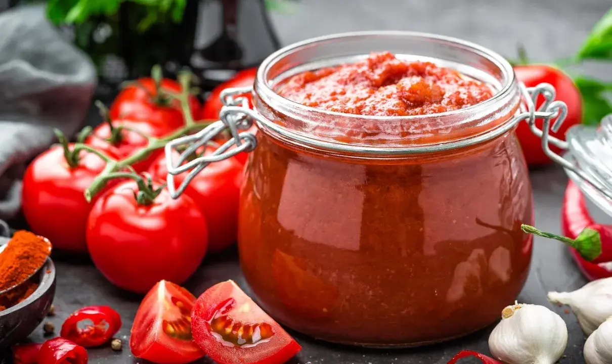 Słoik przecieru pomidorowego, świeże pomidory, czosnek i papryczki chili. Pasteryzacja przecieru pomidorowego w piekarniku to świetny sposób na jego przechowywanie.
