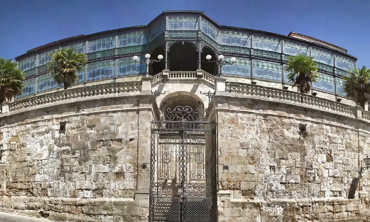 Edificio modernista en Salamanca con niños, palmeras y un cielo azul.