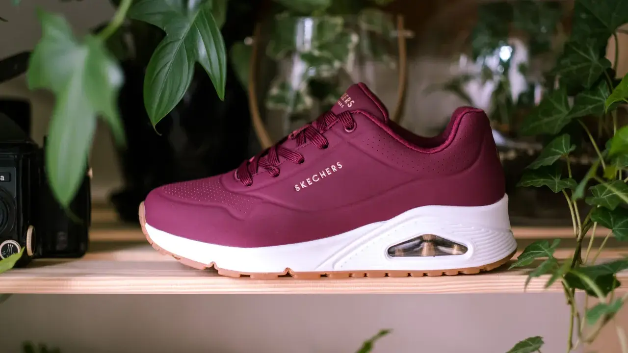 Bordowy but Skechers z białym spodem i brązową podeszwą, otoczony zielonymi liśćmi. Dowiedz się, jak wyczyścić sznurówki, aby buty wyglądały jak nowe.