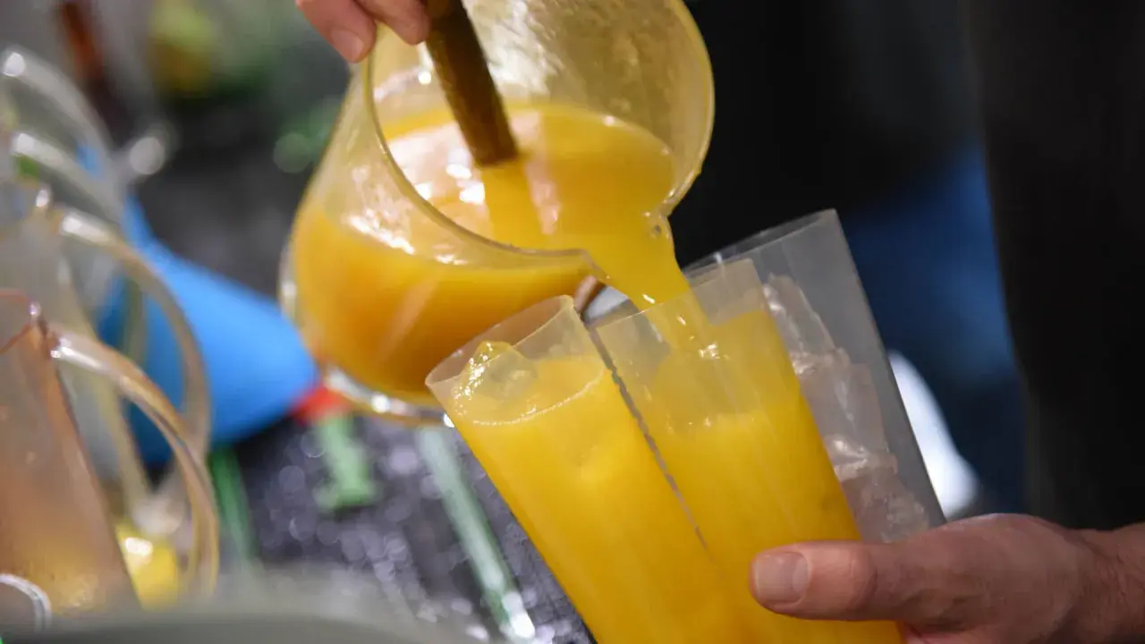 Ein Mann gießt leuchtend gelben Saft, vielleicht Poncha Madeira, aus einer Glaskaraffe in zwei Gläser mit Eiswürfeln.