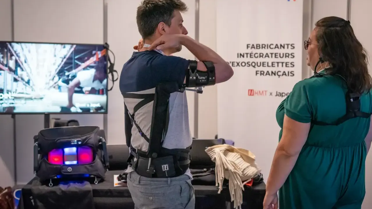 Un homme teste un exosquelette pour le bras, une technologie d'assistance pour le handicap. Une femme observe.