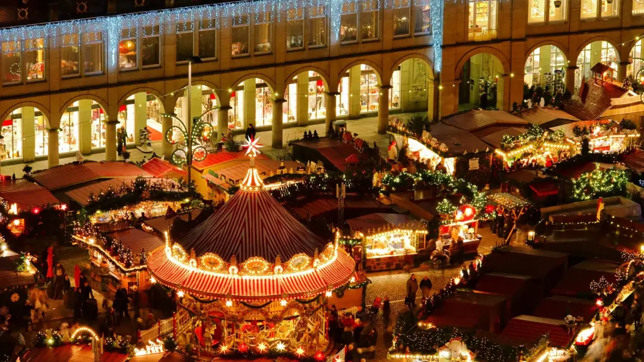 Vista aérea de mercadillos navideños iluminados, con un carrusel festivo y puestos de comida.