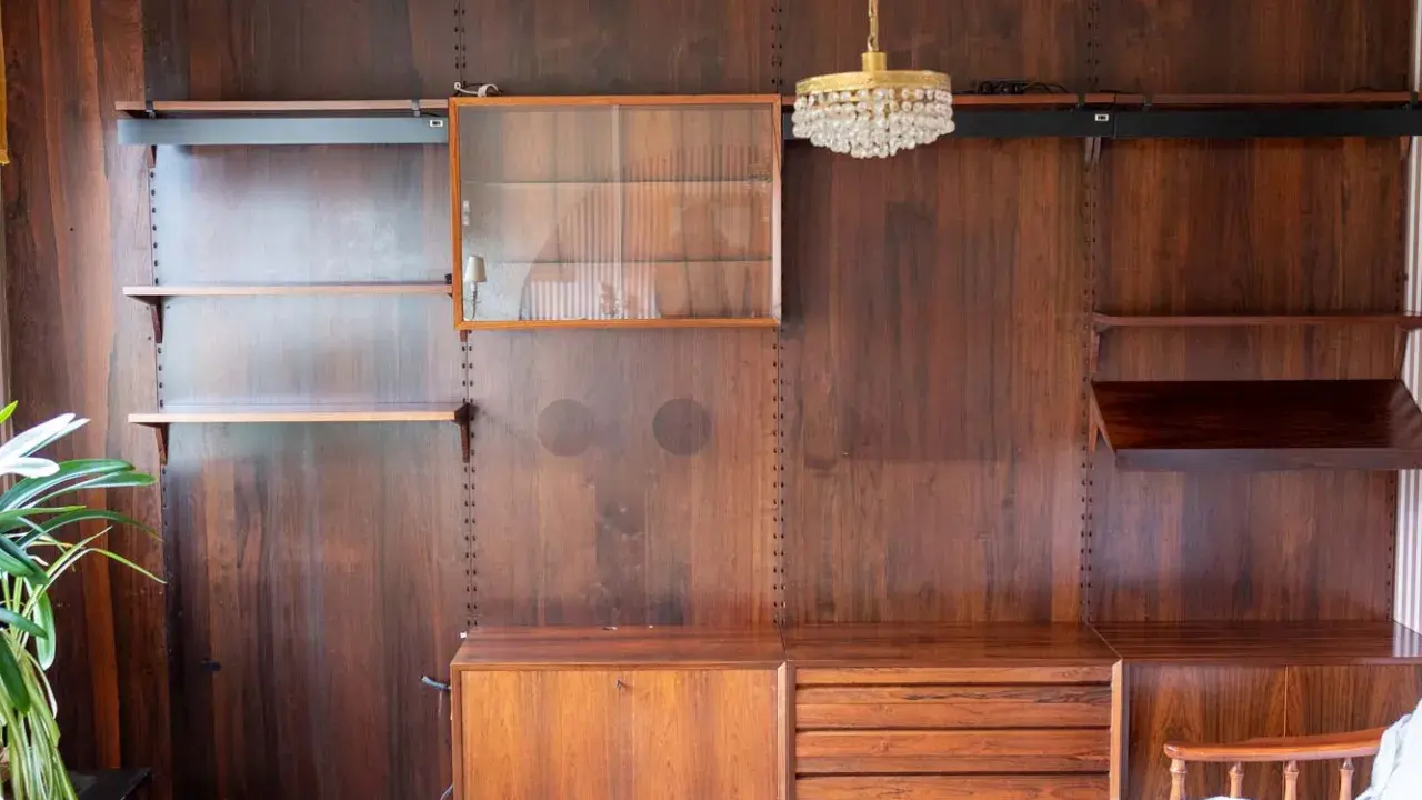 En väggmonterad hylla i teak, troligen designad av Poul Cadovius, med glasmonter, lådor och hyllplan.