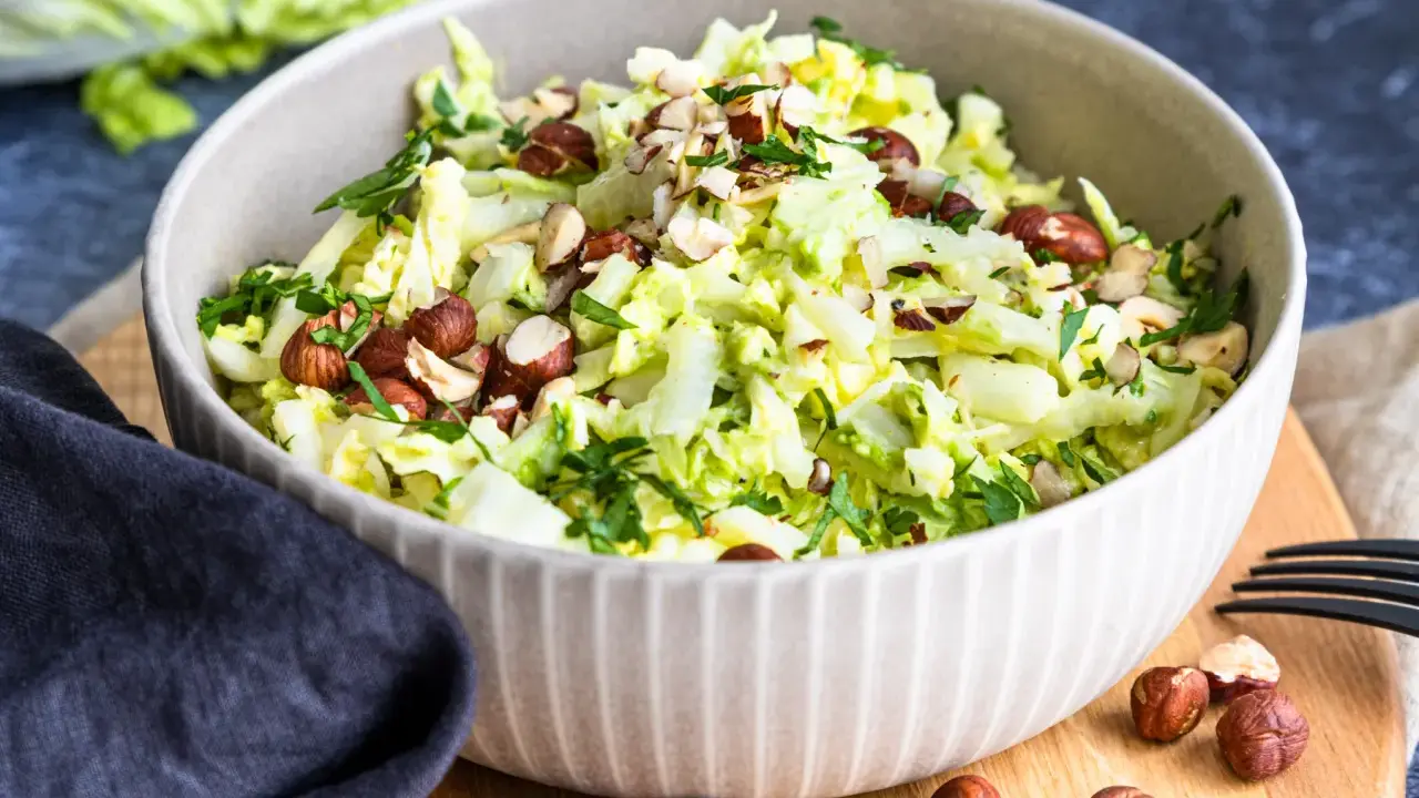 Frischer Chinakohlsalat mit gehackten Haselnüssen und Petersilie, serviert in einer Schüssel.