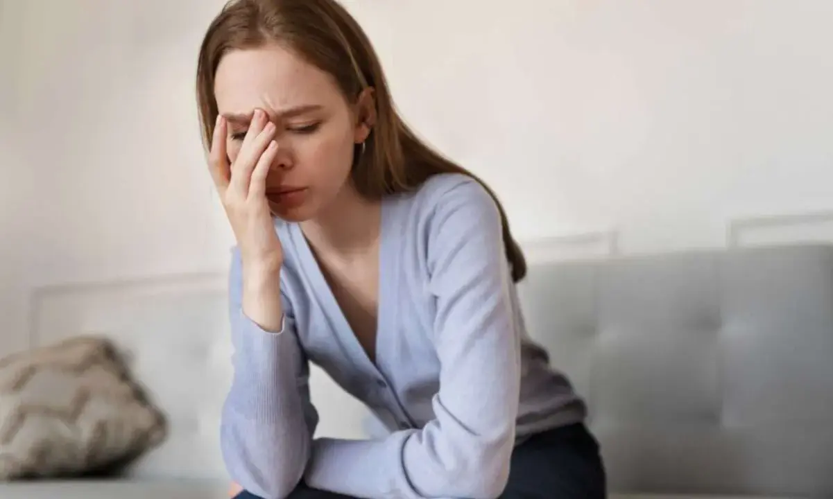 En kvinna sitter på en soffa med handen mot pannan, uttrycker smärta och utmattning i akut fas.