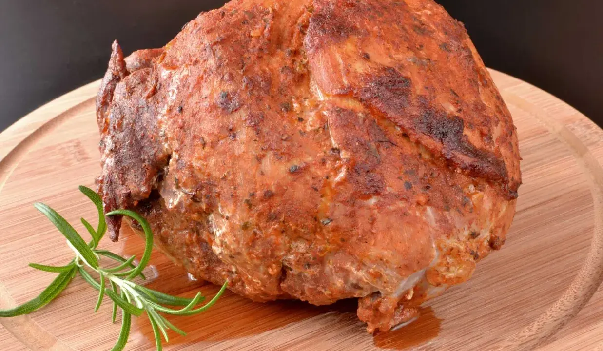 Pieczona szynka z ziołami, która wygląda jakby była przygotowana z użyciem marynaty do szynki. Gałązka rozmarynu dodaje aromatu.