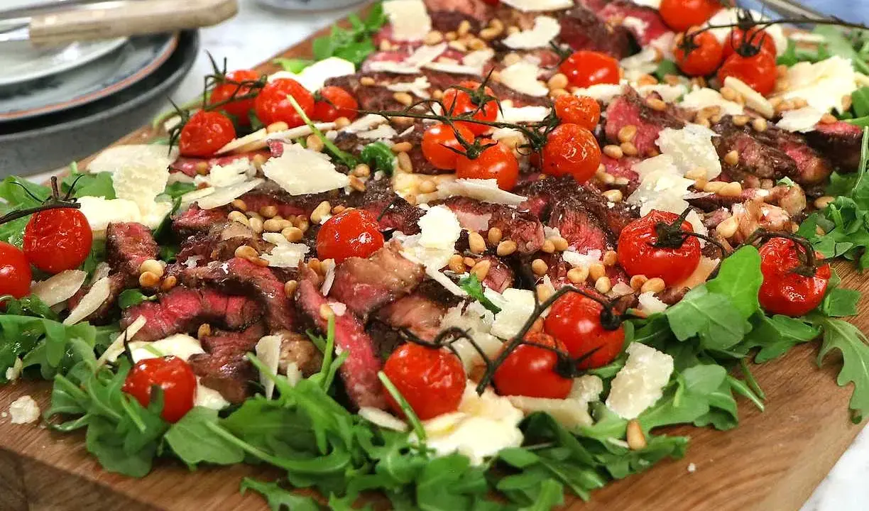 En läcker biff tagliata med körsbärstomater, pinjenötter och parmesan på en bädd av rucola.