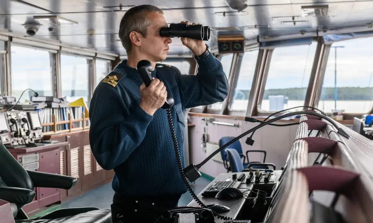 Un officier de marine, comment s'appelle la personne qui conduit un bateau, utilise des jumelles et un téléphone dans la passerelle.