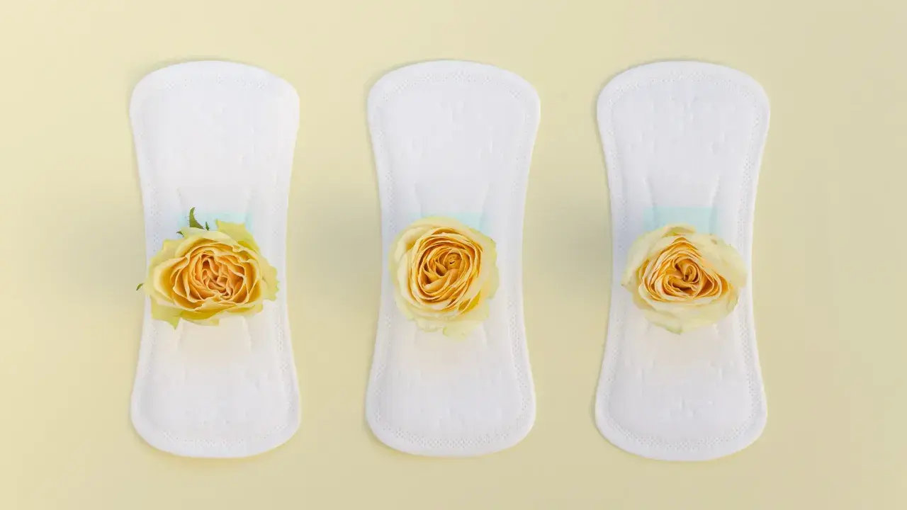Tres compresas blancas con delicadas rosas amarillas, simbolizando un flujo escaso y la delicadeza del cuidado personal.
