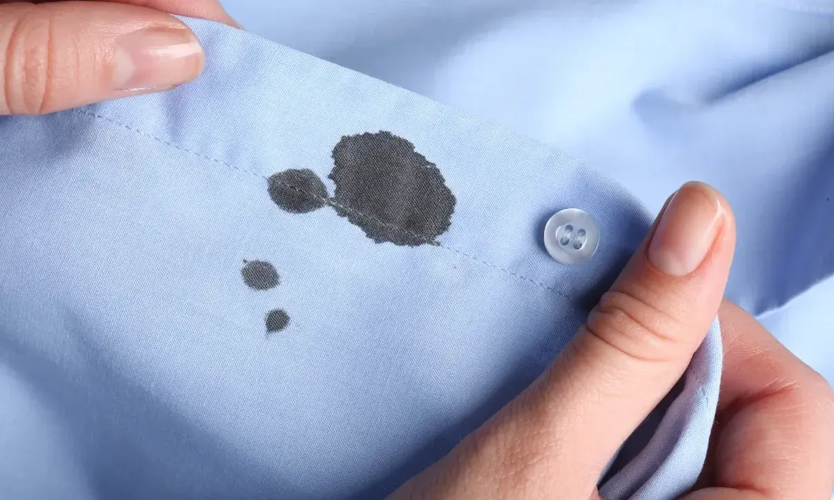 Manos sostienen camisa azul con manchas de bolígrafo. Aprende como quitar manchas de bolígrafo en ropa.
