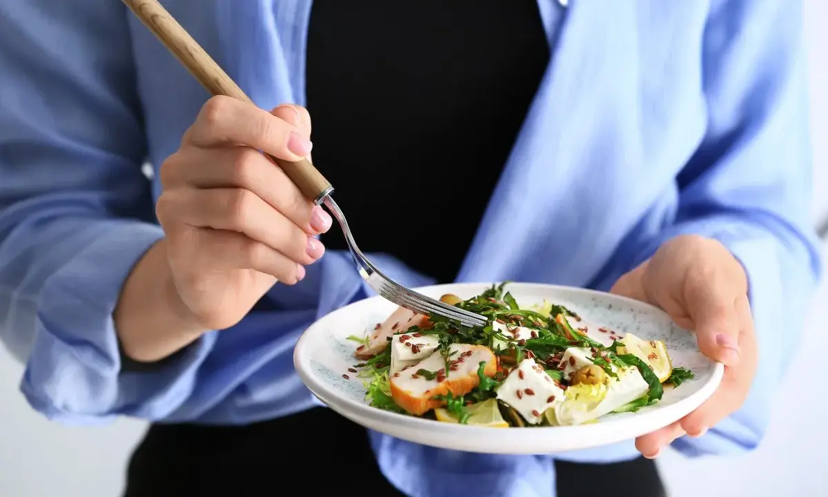 Kobieta je sałatkę z kurczakiem i serem feta, idealną na dietę 1200 kcal.