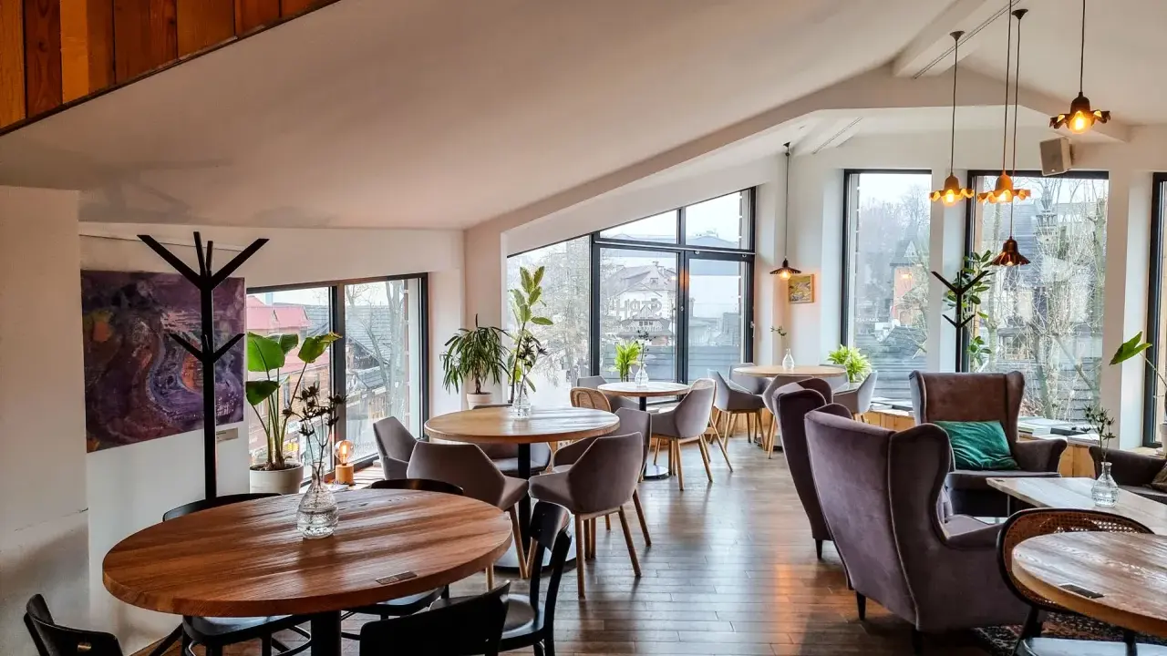 Przytulna restauracja w Bukowinie Tatrzańskiej z widokiem na góry. Drewniane stoły, wygodne fotele i stylowe oświetlenie tworzą ciepłą atmosferę.
