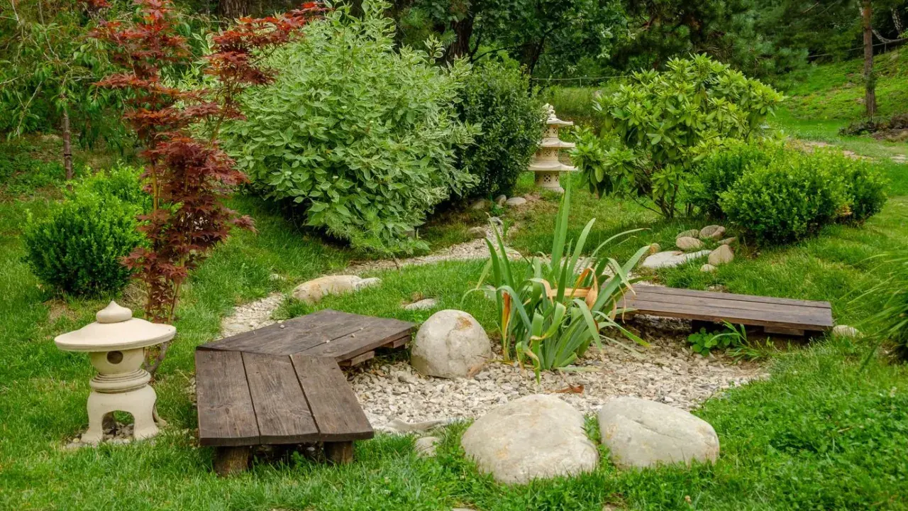 Un paisible petit jardin japonais avec des lanternes, des bancs en bois, des rochers et une végétation luxuriante.