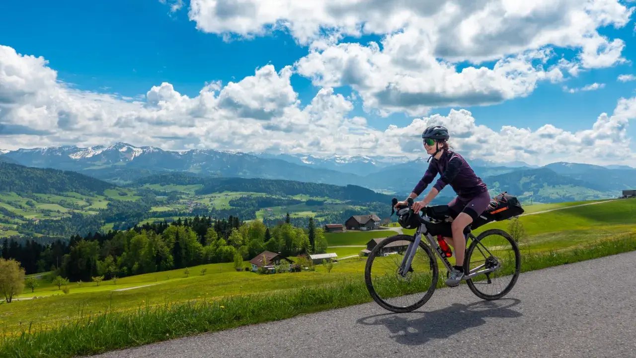 Frau fährt mit Bikepacking-Ausrüstung auf einer Straße mit Alpenpanorama.