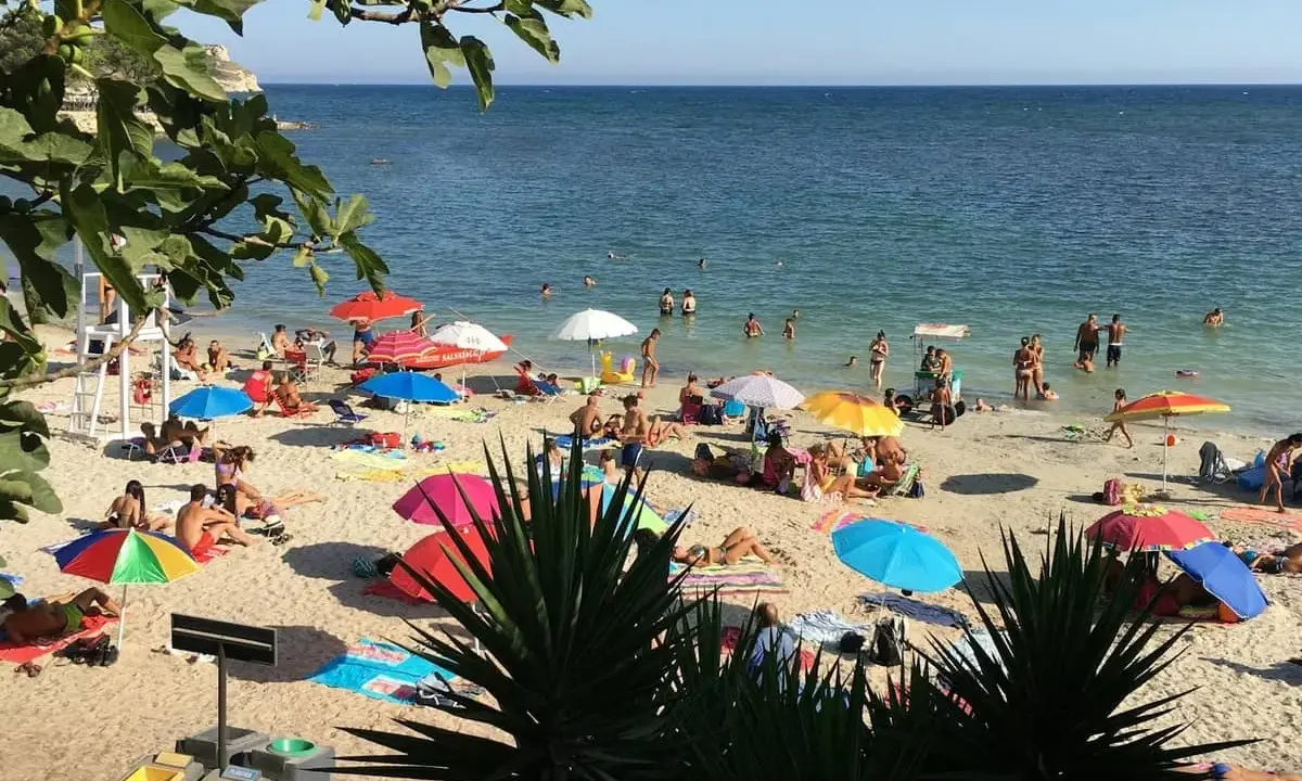 Playa de Cerdeña con niños jugando y familias disfrutando del sol bajo sombrillas coloridas.