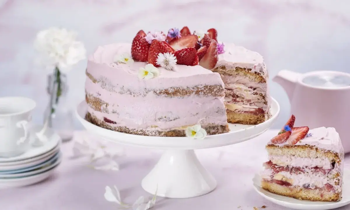En vacker jordgubbstårta med rosa frosting och färska jordgubbar. En bit är uppskuren och ligger på en separat tallrik.