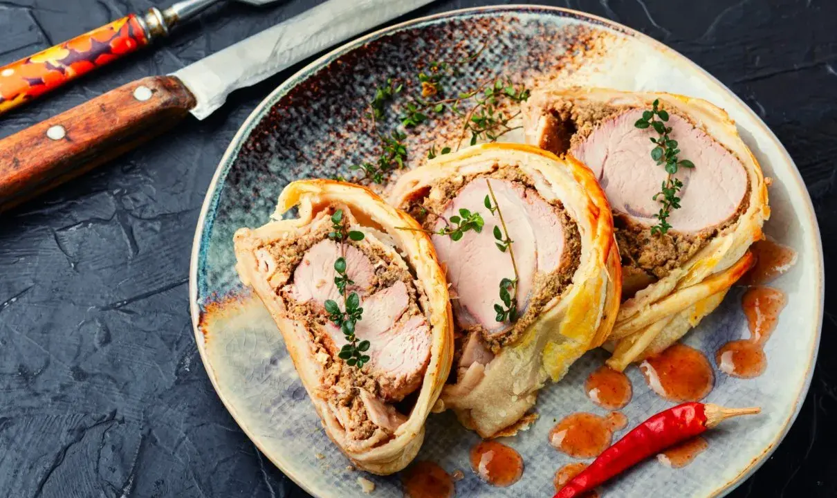Pyszne danie z ciasta francuskiego z soczystym mięsem i farszem grzybowym, udekorowane gałązkami tymianku i papryczką chili.