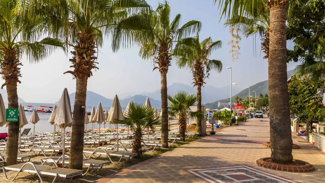 Alejka z palmami prowadzi do plaży w Marmaris, Turcja. Leżaki i parasole czekają na turystów.