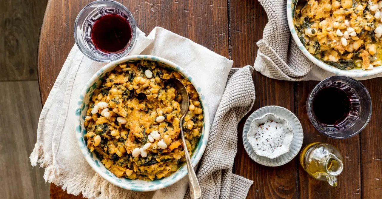Un piatto rustico di fagioli e verdure, perfetto per scoprire cosa mangiare in Toscana. Accompagnato da vino rosso e olio d'oliva.