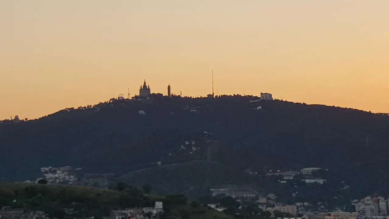 Silhouetten von Gebäuden auf einem bewaldeten barcelona berg im Abendlicht.