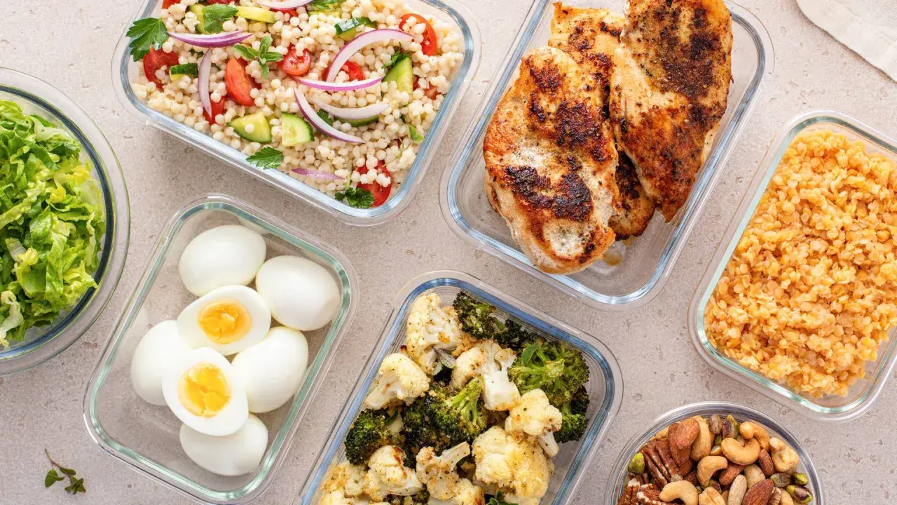 Förberedd student mat i glasbehållare: kycklingfilé, couscoussallad, grönsaker, ägg och nötter. Perfekt för en hälsosam lunchlåda.