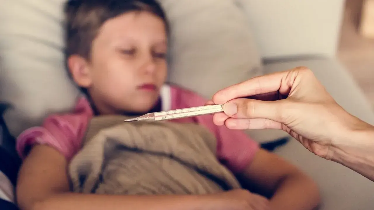 Dziecko z gorączką, czuć zimne rączki i nóżki. Mama mierzy temperaturę termometrem.
