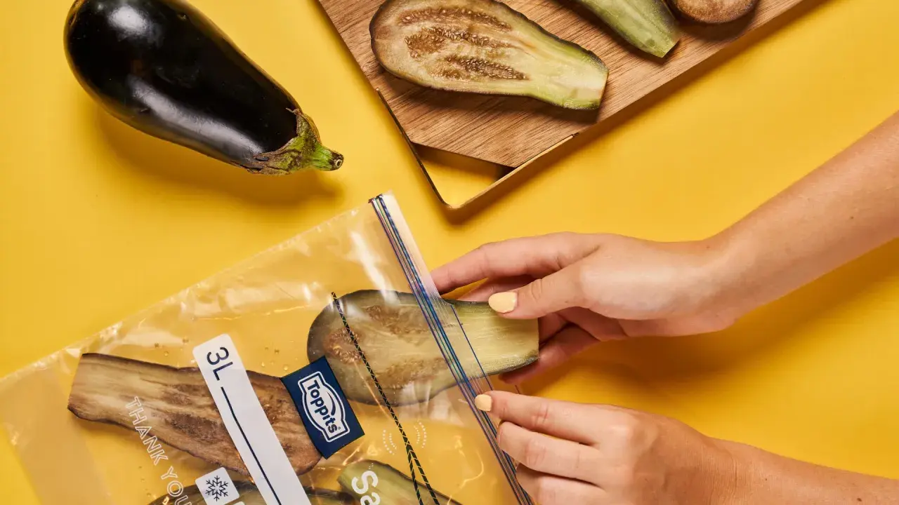 Hände legen Auberginenscheiben in einen Gefrierbeutel. So einfach ist das Aubergine einfrieren für später.