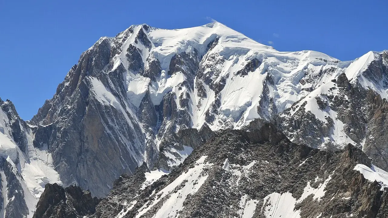 Majestatyczny, ośnieżony szczyt, gdzie jest Mont Blanc, góruje nad skalistym, pokrytym śniegiem zboczem.