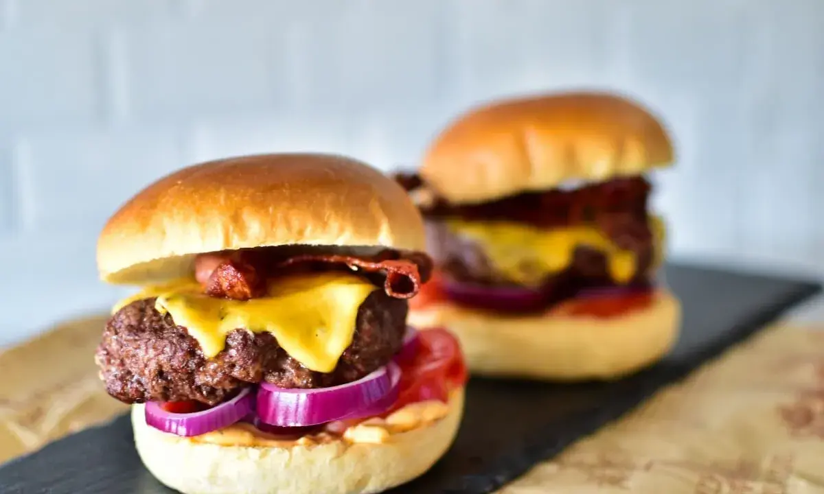 Zwei saftige Burger im Airfryer zubereitet, mit geschmolzenem Käse, knusprigem Speck und roten Zwiebeln.