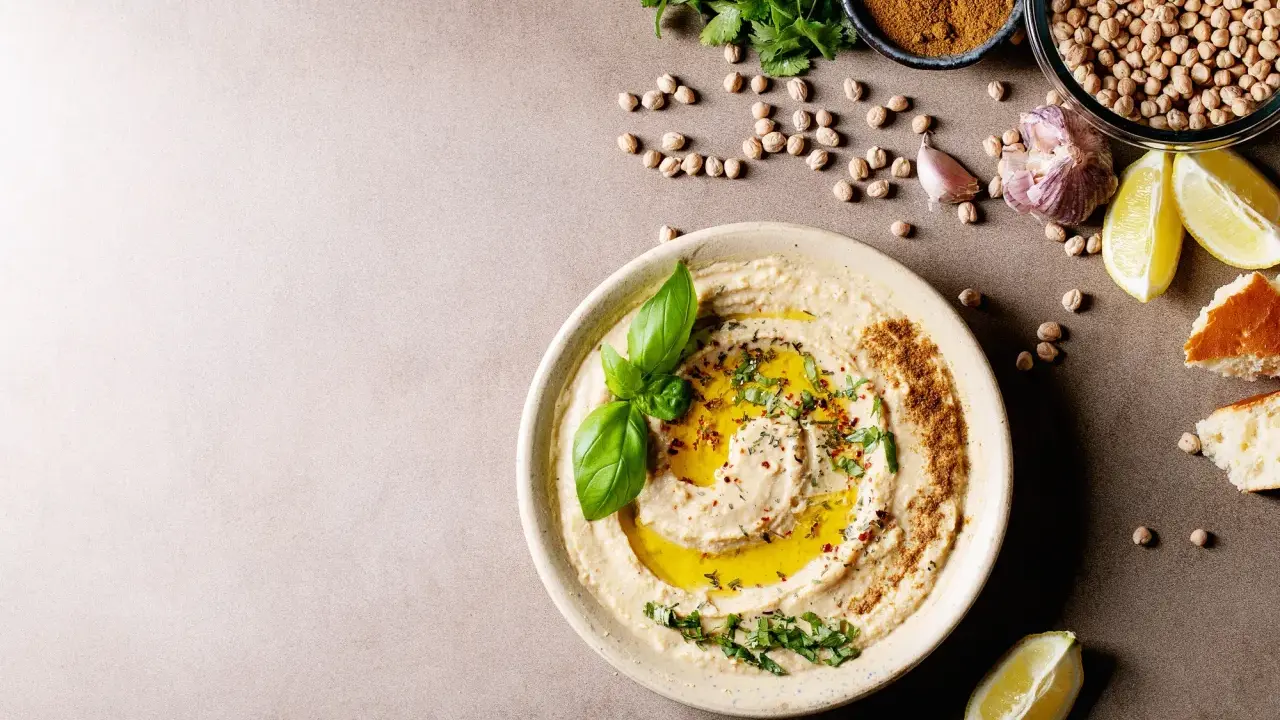 Pyszny hummus z oliwą, ziołami i bazylią. Obok ciecierzyca, czosnek, cytryna i chleb. Czy można mrozić hummus? Tak, można go mrozić.