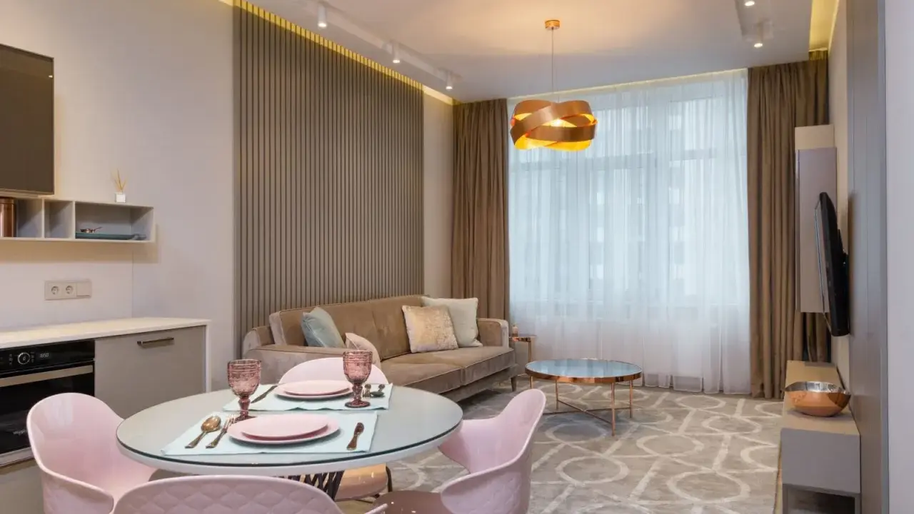 Nowoczesny salon z aneksem kuchennym po generalnym remoncie mieszkania 50m2. Jasne kolory, welurowa sofa i różowe krzesła tworzą przytulną atmosferę.