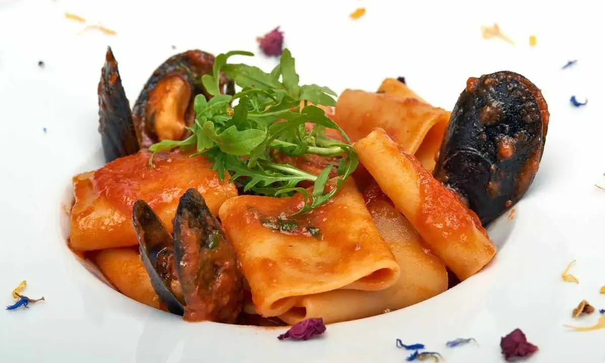 Paccheri allo scoglio con cozze e pomodoro, guarniti con rucola fresca e petali di fiori.