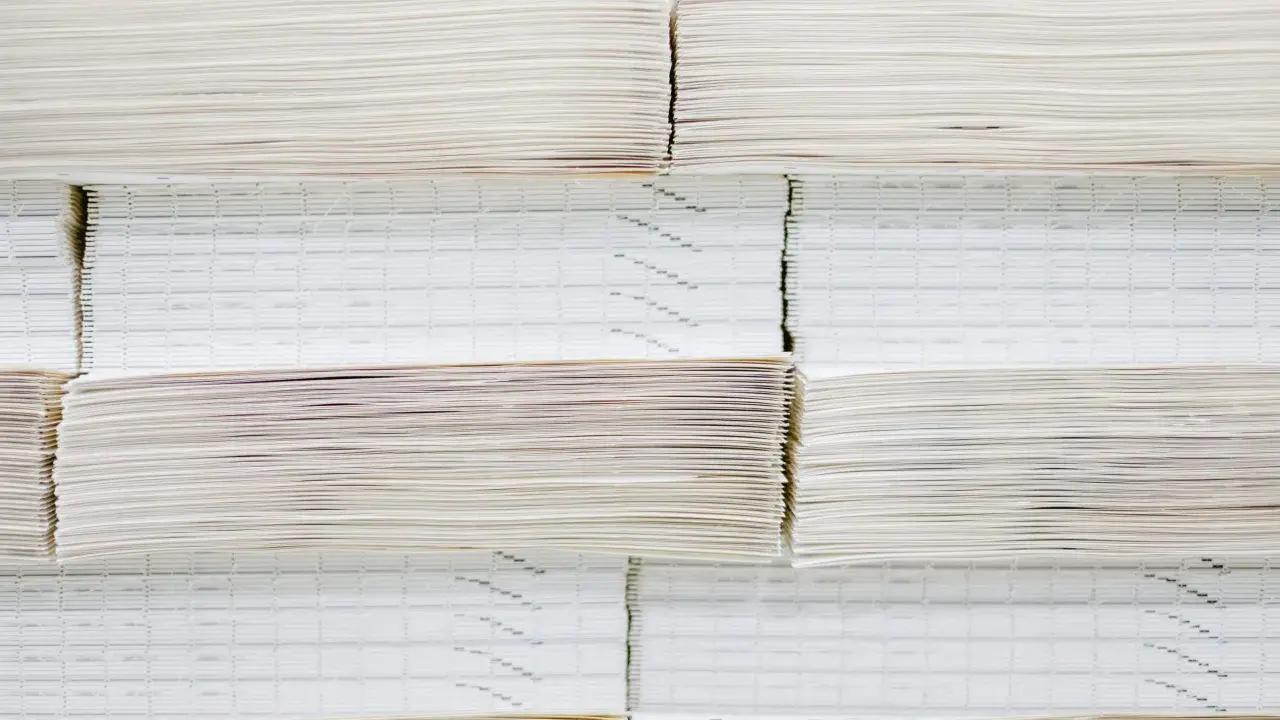 Grandes pilas de papel offset, algunas con finas líneas impresas, apiladas ordenadamente en un almacén.