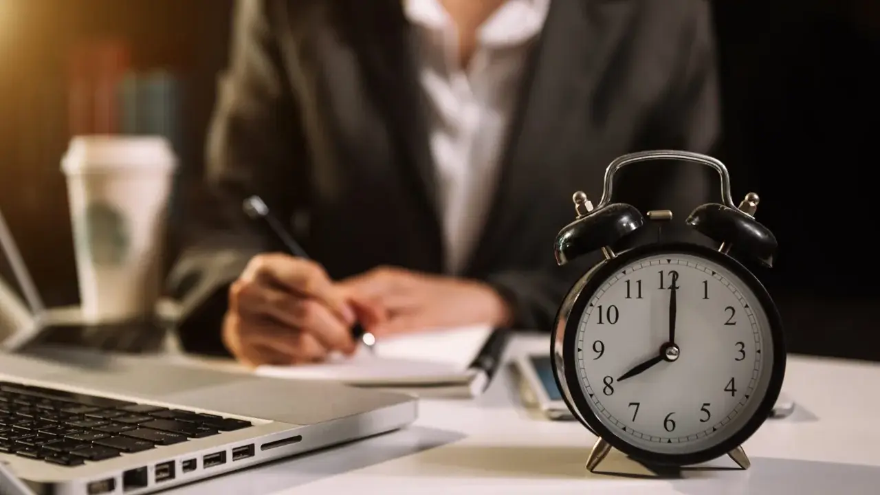 Zegar pokazuje 8:00. Zastanawiasz się, ile to godzin przy pracy na 1/2 etatu? Obok laptop, notatnik i kawa.
