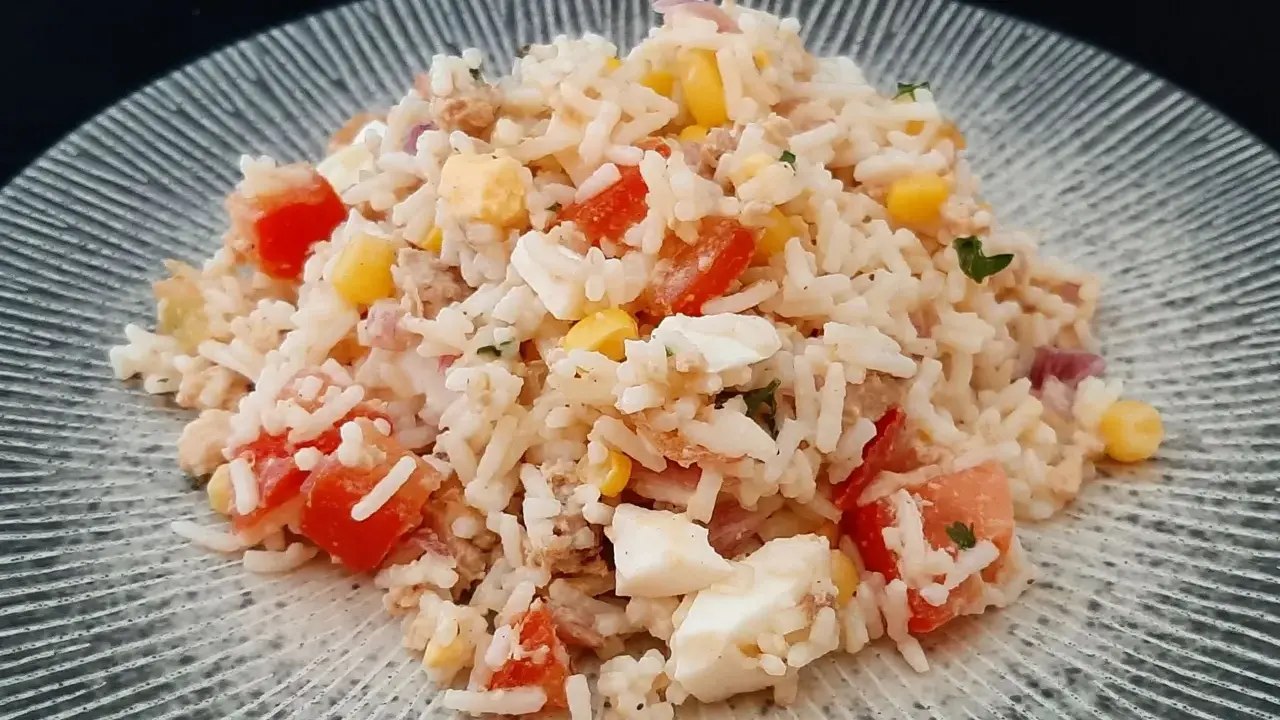 Salade de riz, thon, tomates, maïs et œuf dur sur une assiette grise.