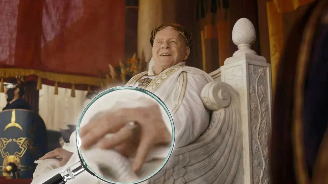 Ein Mann mit Lorbeerkranz, der an alle Kaiser Roms erinnert, sitzt auf einem Thron. Eine Lupe enthüllt Details seiner Hand.