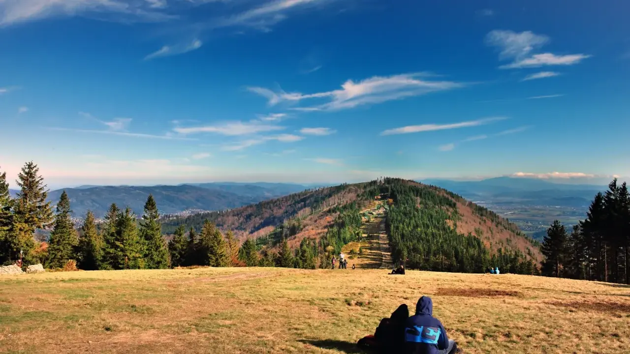 Widok na góry w Bielsku-Białej. Dwie osoby siedzą na trawie, podziwiając jesienny krajobraz i panoramę Beskidów.
