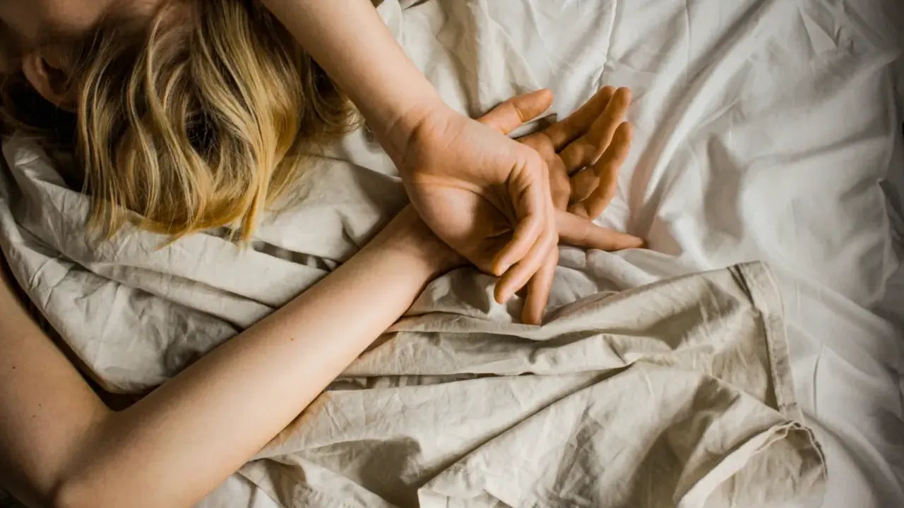 Blonde Haare auf einem Kissen, Arme schlafen nachts ein, Hände ruhen auf der Decke.