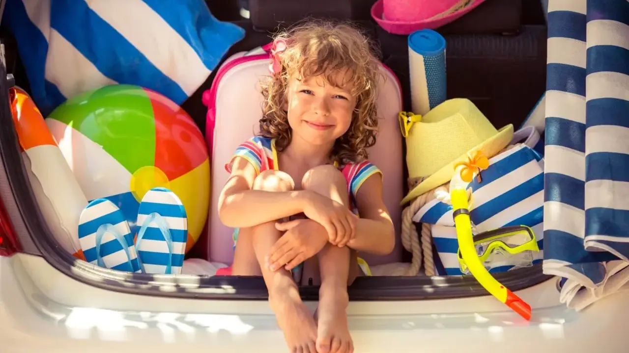 Niña sonriente rodeada de artículos de playa, lista para explorar nuevos sitios para ir con niños.