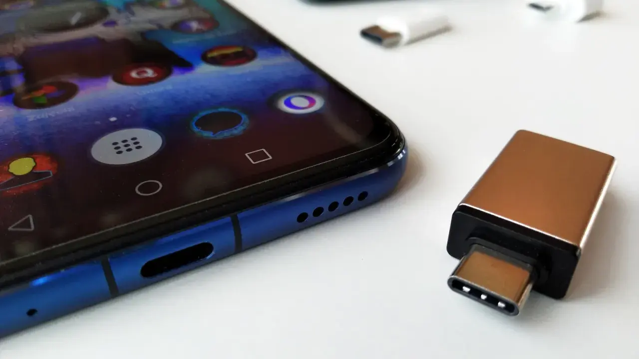 Złoty adapter USB-C i białe przejściówki leżą obok niebieskiego smartfona. Dowiedz się, jak podłączyć pendrive do telefonu.