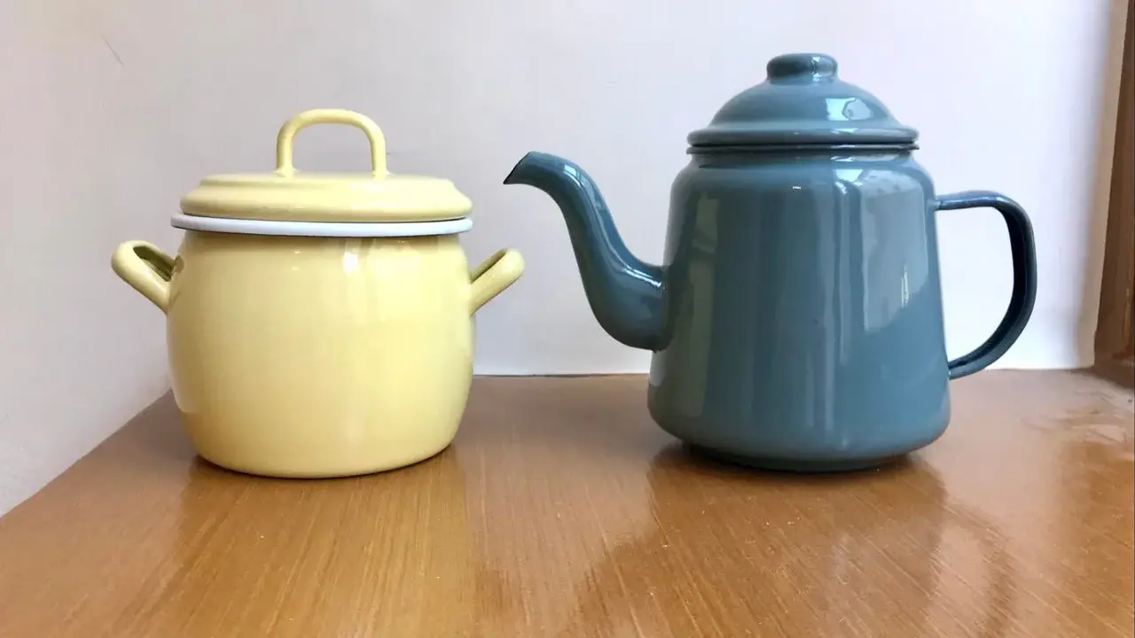 En gul gryta och en blå kaffepanna i emalj, liknande en klassisk kockums kaffepanna, står på ett träbord.