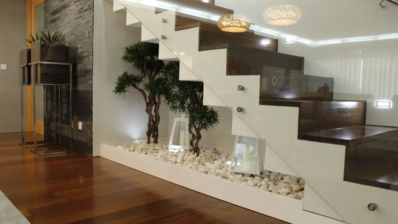 Elegante subida de escalera interior con plantas decorativas y piedras blancas.