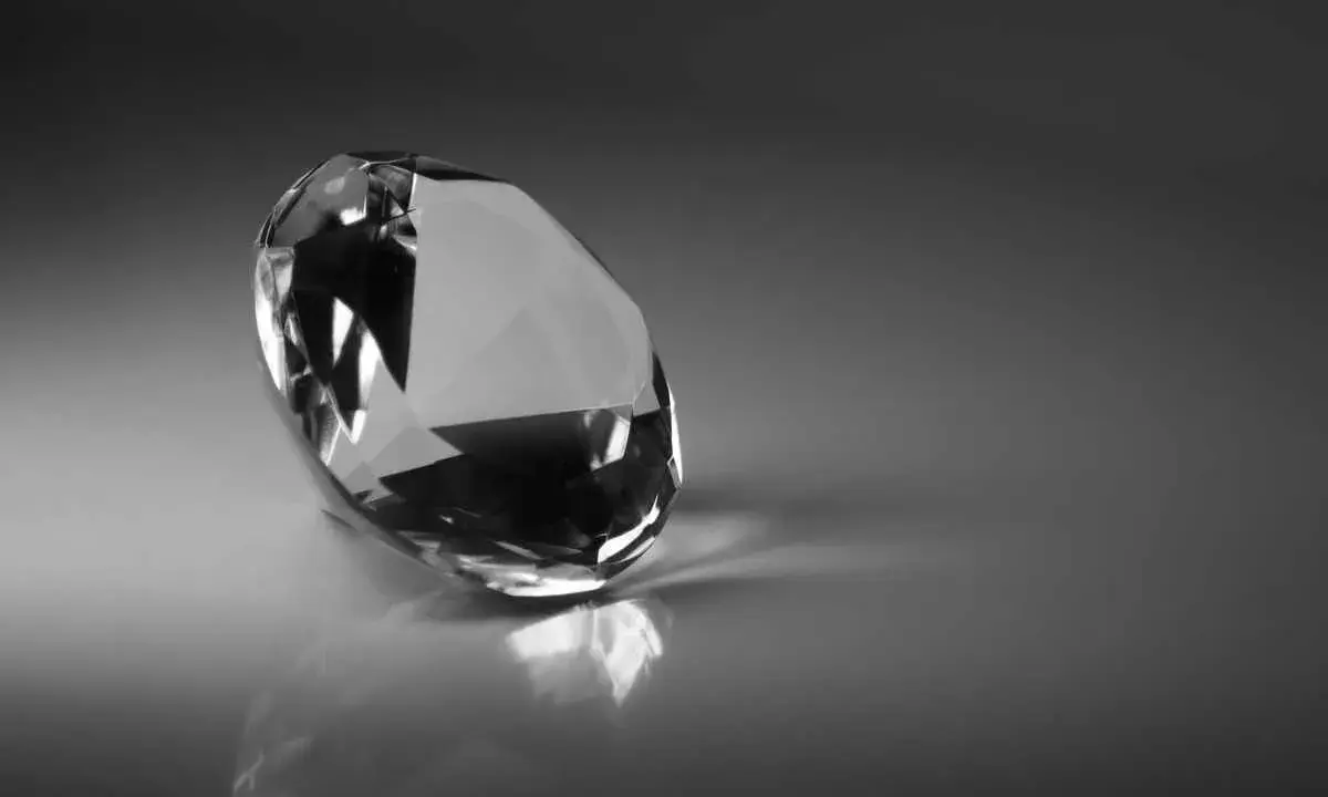 Un diamante sfaccettato riflette la luce su una superficie lucida. Il suo fascino misterioso evoca il significato dei diamanti neri: forza e resilienza.