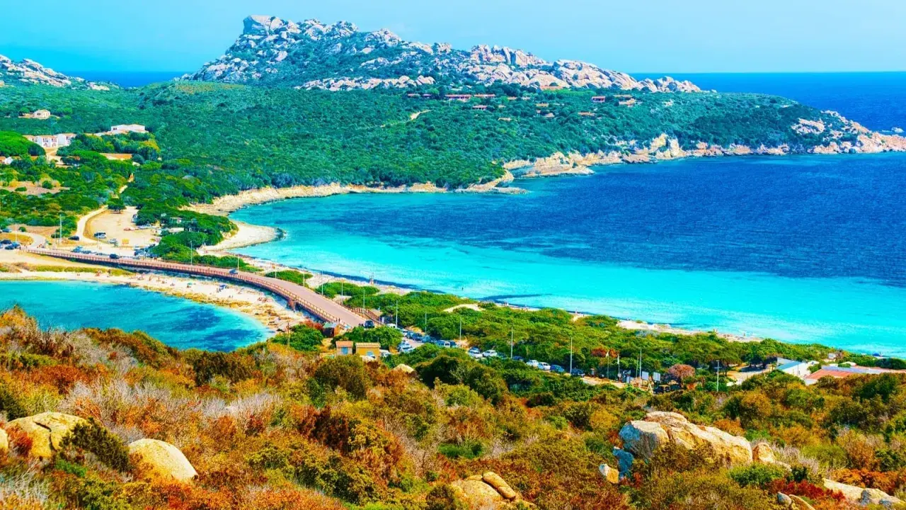 Vacker kustlinje med turkost vatten, en bro och gröna kullar. En dröm för en **Sardinien resa**.