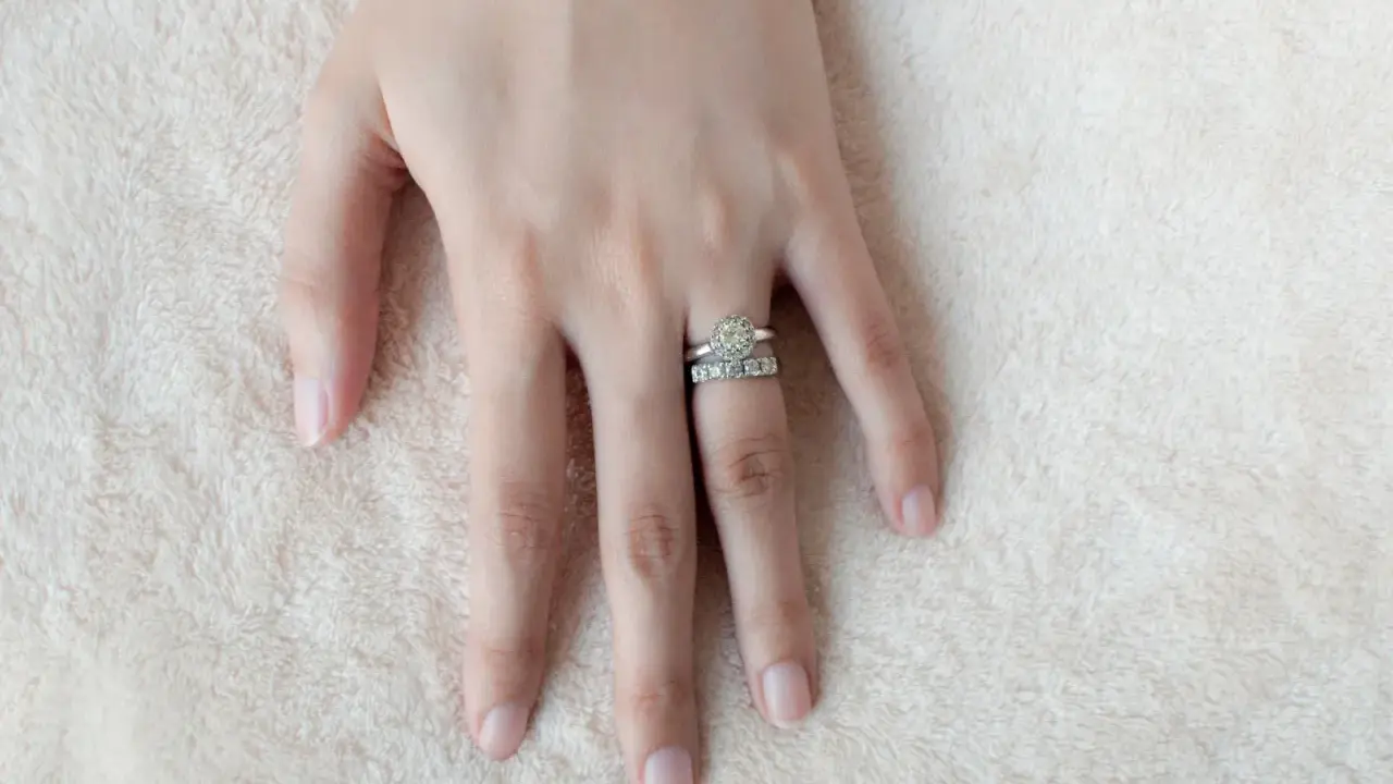 Mano femminile con due anelli scintillanti, uno con un grande diamante centrale e l'altro con pietre più piccole. Il dito anulare è il posto tradizionale dove si mette l'anello di fidanzamento donna.