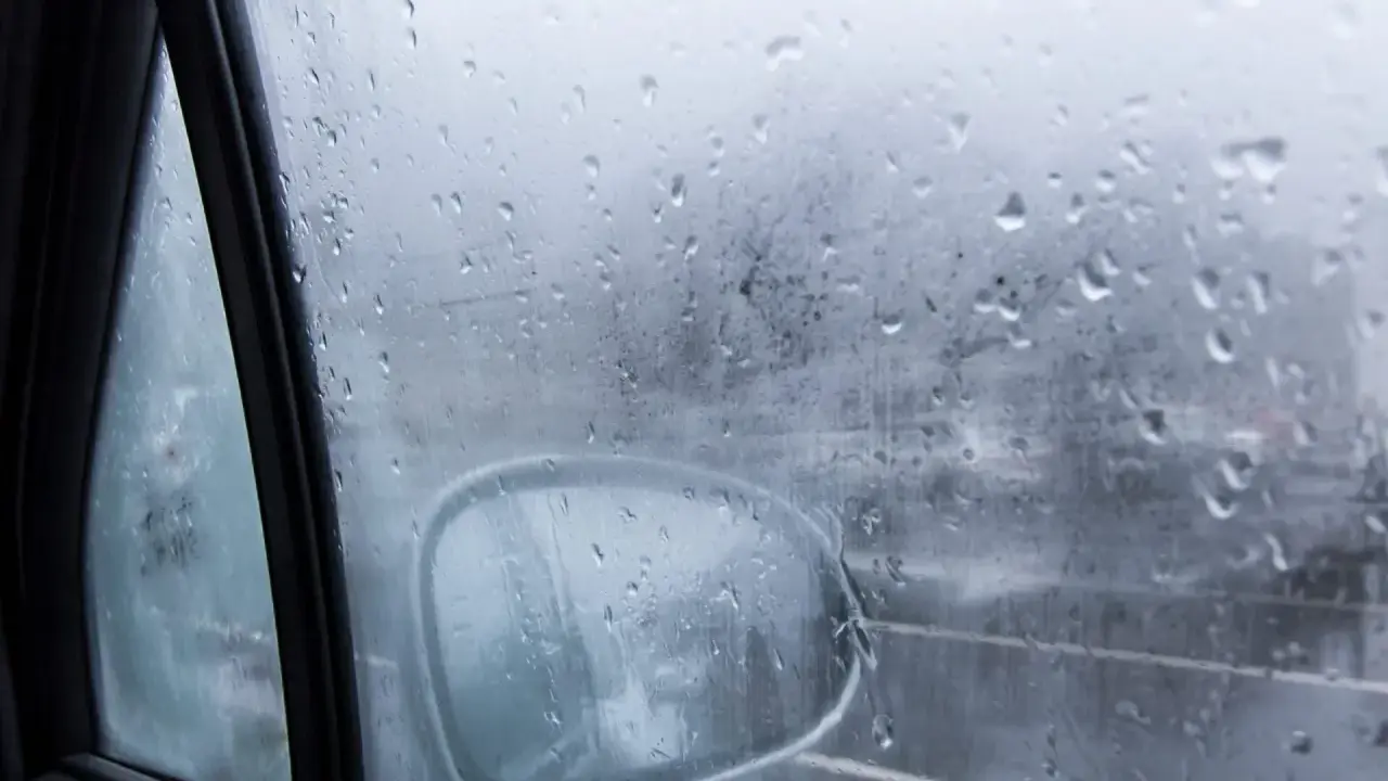 Gotas de lluvia en el cristal del coche, reflejando el exterior y el espejo retrovisor. Una escena que explica porque se empañan los cristales en días húmedos.