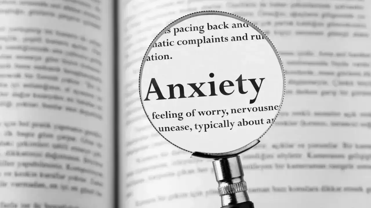 Lupa powiększa definicję "Anxiety" w książce, opisując uczucie niepokoju, które może prowadzić do fobi.